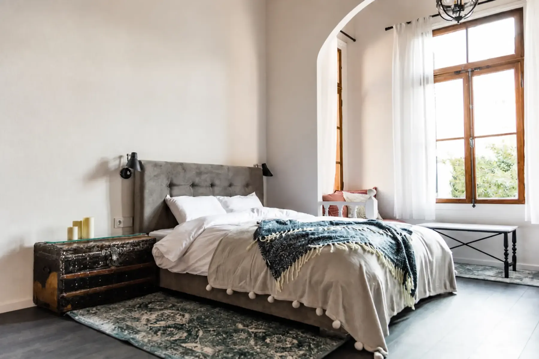 Bright bedroom with an upholstered headboard, white linen and an arched window