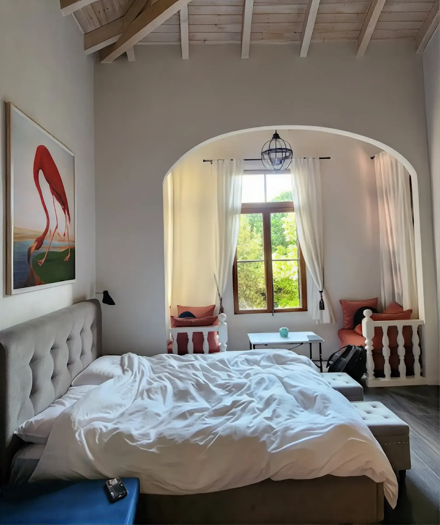 Bedroom with a double bed under an arched window and cushioned window seats