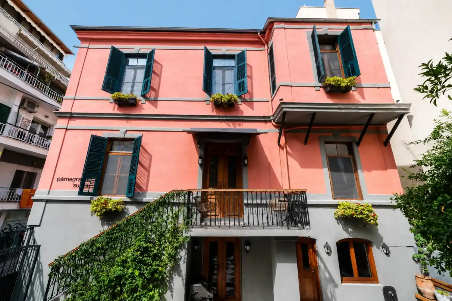 Front facade of PomeGranate Suites with teal shutters, flower boxes and a balcony above the entrance