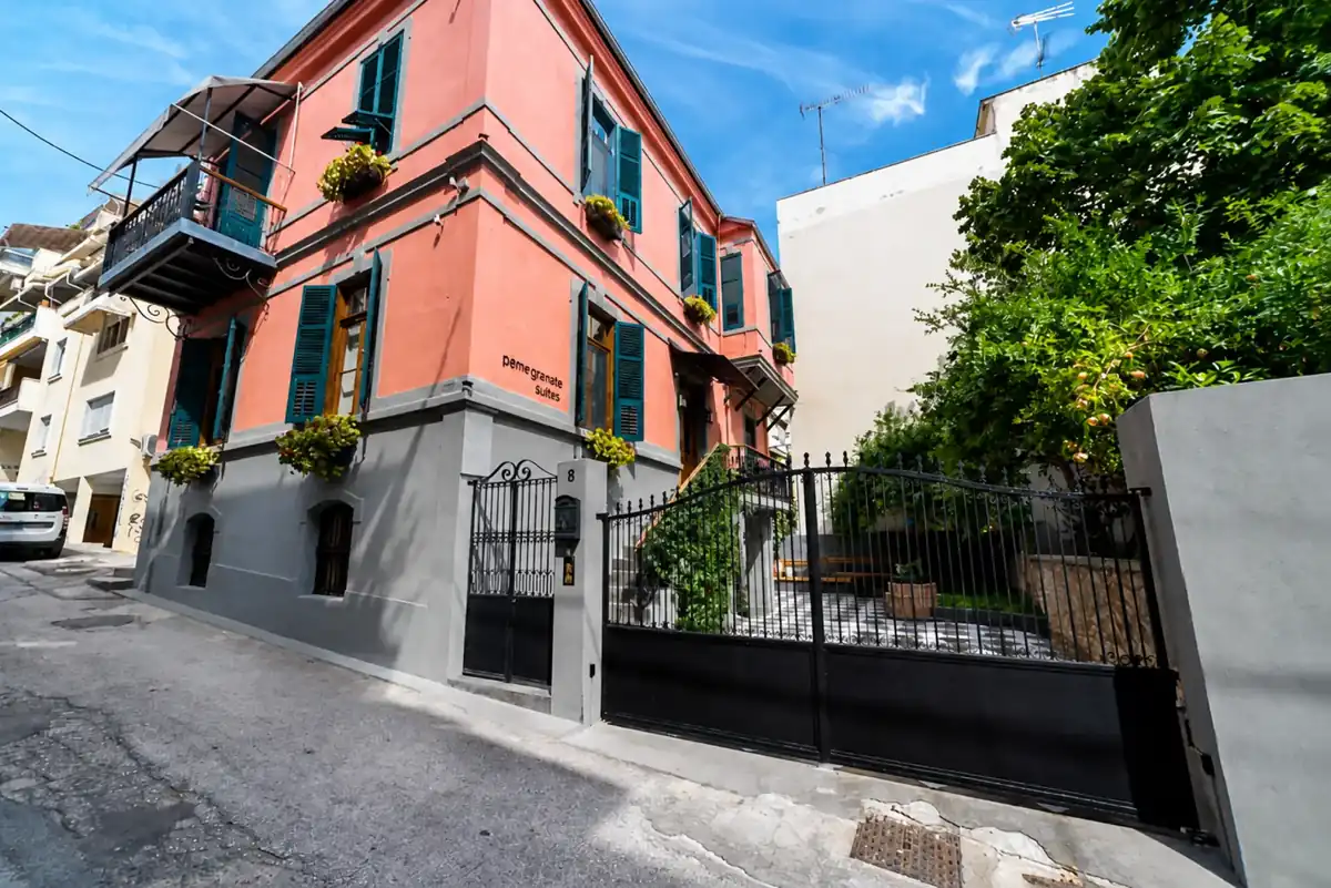 Corner view of the coral-painted PomeGranate Suites building with its iron gate and pomegranate tree